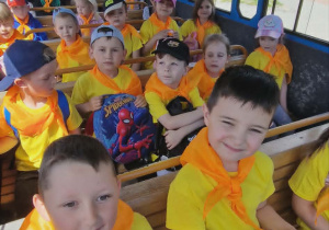 Dzieci siedzą w wagonie kolejki, która jedzie po terenie zoo