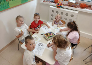 Dzieci siedzą przy stolikach i kolorują obrazki.