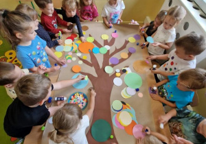 Przedszkolaki wspólnie tworzą drzewo z kolorowych kropek.