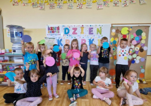 Dzieci trzymają kolorowe kropki i pozują do zdjęcia grupowego.