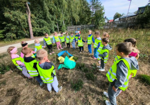 Przedszkolaki stoją w kole i przypominają zasadę segregowania śmieci do odpowiednich worków.
