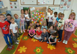 Dzieci pozują do zdjęcia i prezentują drzewo życzliwości wykonane z kolorowych dłoni.