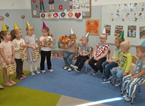 Dziewczynki śpiewają sto lat chłopcom, którzy siedzą na krzesłach