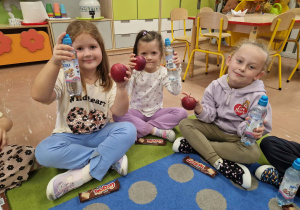 Dzieci siedzą w sali i trzymają wodę i jabłko