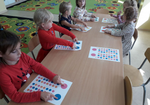 Dzieci siedzą przy stolikach podczas zabawy "Kodowanie z kropką",