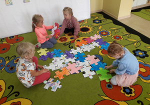 Dzieci na dywanie układają puzzle.