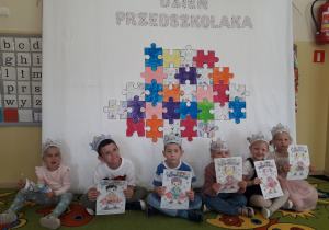 Przedszkolaki pozują na tle dekoracji Dzień Przedszkolaka.