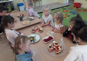 Dzieci siedzą przy stolikach, na których rozłożone są różne owoce.