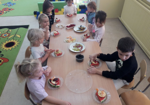 Dzieci przy stolikach degustują wykonane owocowe pizze.