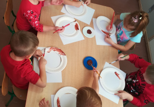 Dzieci przy stoliku malują farbami.