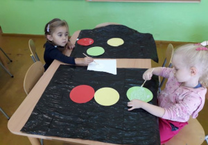 Dwie dziewczynki naklejają kolorowe kółka na sygnalizator.