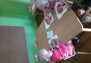 Dzieci przy stolikach malują farbami jeża.