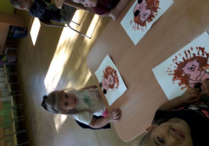 Dzieci przy stolikach malują farbami jeża.