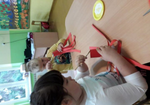 Dzieci przy stoliku wykonują jesienne jabłko z czerwonej kartki.