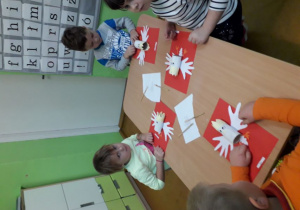 Dzieci wykonują godło Polski z białoczerwonych kartek i rolki papieru.