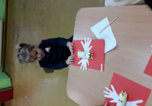 Dziewczynka wykonuje godło Polski z białoczerwonych kartek i rolki papieru.