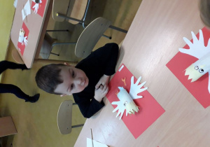 Chłopiec wykonuje godło Polski z białoczerwonych kartek i rolki papieru.
