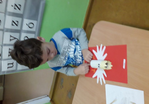 Chłopiec wykonuje godło Polski z białoczerwonych kartek i rolki papieruu.